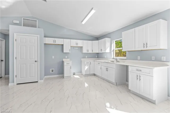 Kitchen featuring white cabinets, light countertops, vaulted ceiling, and light marble finish floors