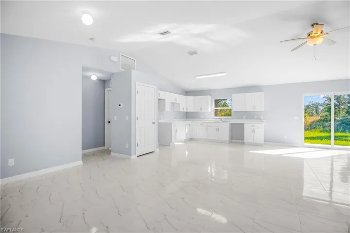 Unfurnished living room featuring ceiling fan, light marble finish flooring, and lofted ceiling