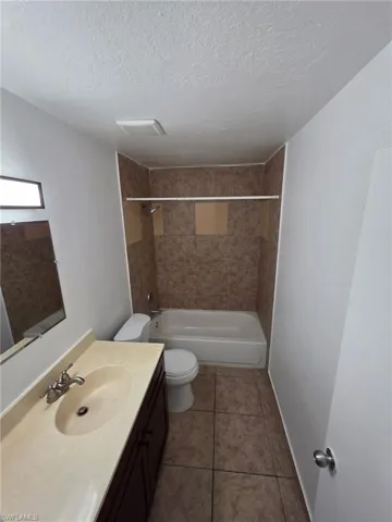 Bathroom with vanity, a textured wall, a textured ceiling, shower / washtub combination, and light tile patterned floors