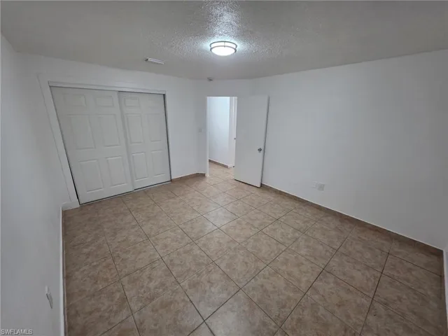 Unfurnished bedroom with a textured ceiling, a closet, and light tile patterned flooring