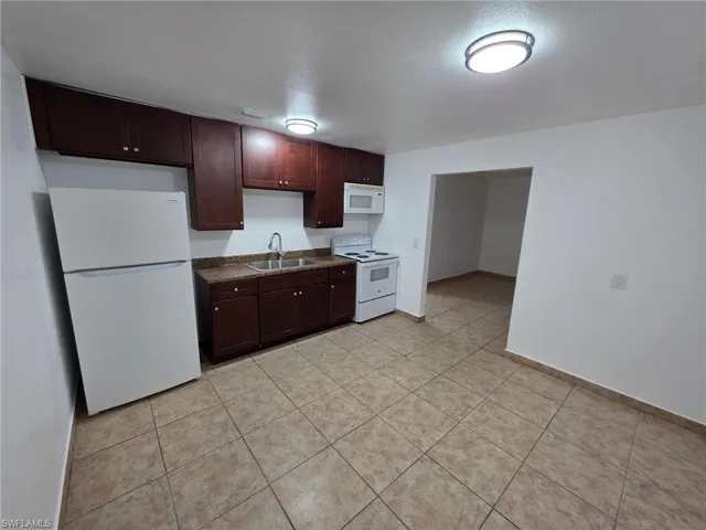 Kitchen featuring white appliances, dark brown cabinetry, dark countertops, light tile patterned flooring, and a textured ceiling