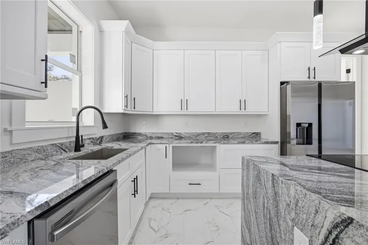 Kitchen with light stone countertops, stainless steel appliances, light marble finish floors, and white cabinets
