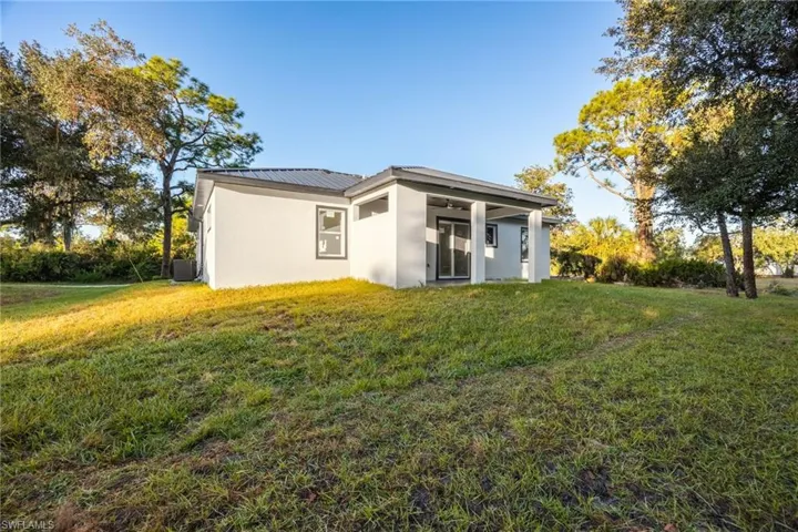 Back of house with a yard, stucco siding, a metal roof, and a patio area