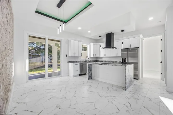 Kitchen featuring a kitchen island, hanging light fixtures, light marble finish flooring, dark stone countertops, and appliances with stainless steel finishes