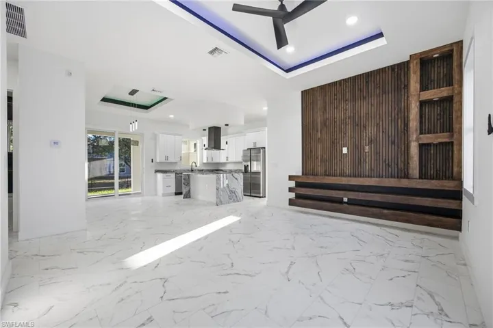Unfurnished living room with a raised ceiling, light marble finish flooring, recessed lighting, and a ceiling fan