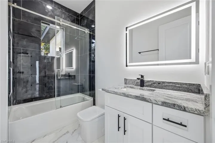 Full bathroom with shower / bath combination with glass door, vanity, and light marble finish flooring