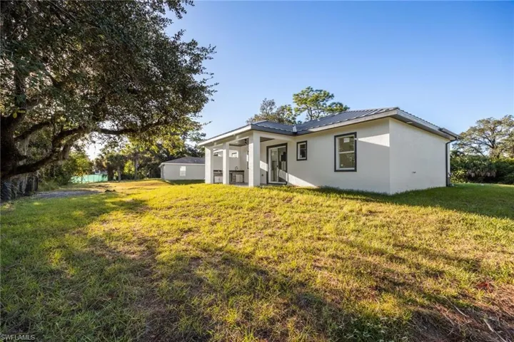 Rear view of house featuring stucco siding, a lawn, a patio, and a metal roof