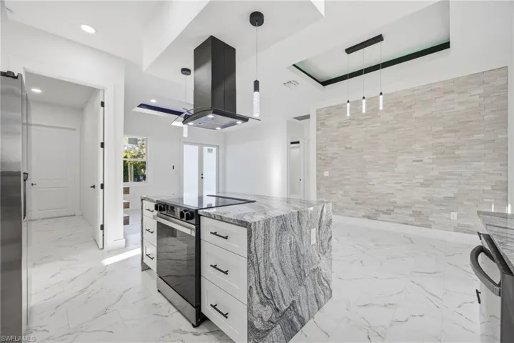 Kitchen with white cabinets, pendant lighting, appliances with stainless steel finishes, island range hood, and light stone counters