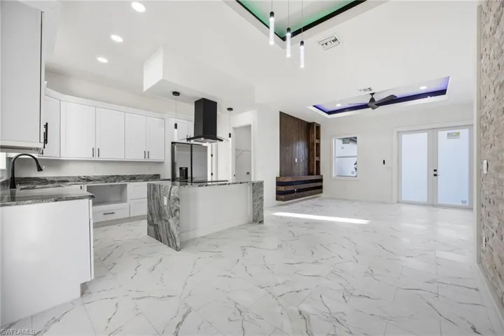 Kitchen with a tray ceiling, white cabinetry, dark stone counters, open floor plan, and extractor fan