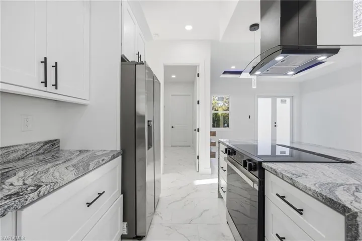 Kitchen featuring island range hood, light stone countertops, black electric range oven, white cabinets, and light marble finish floors
