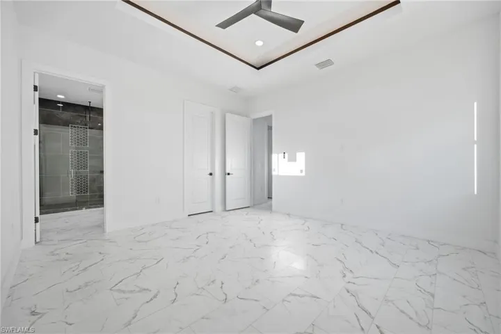 Unfurnished bedroom featuring light marble finish floors, ensuite bathroom, and a ceiling fan