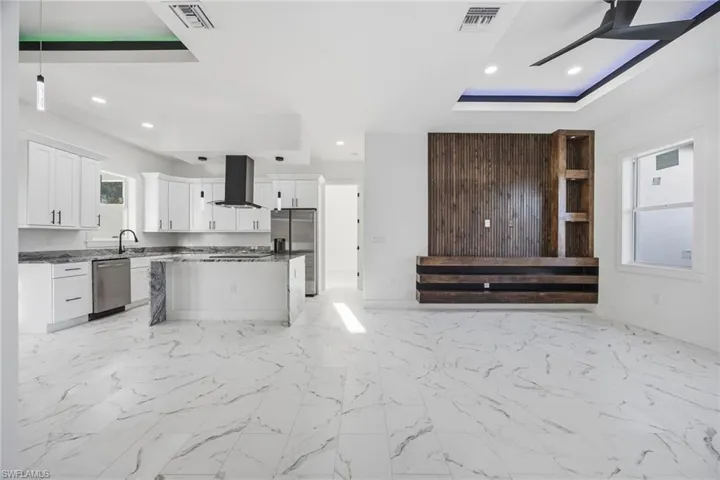 Kitchen featuring open floor plan, light marble finish flooring, a ceiling fan, range hood, and stainless steel appliances