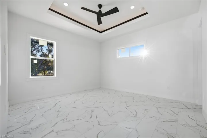 Spare room featuring a tray ceiling, light marble finish floors, ceiling fan, and recessed lighting