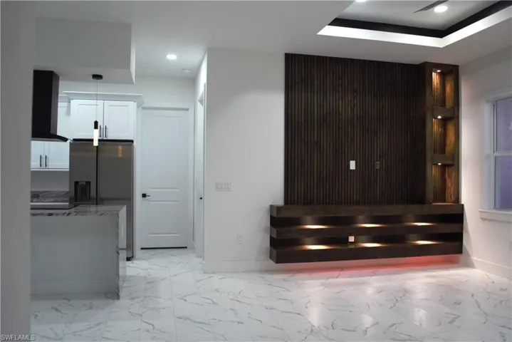 Kitchen with stainless steel refrigerator with ice dispenser, light stone counters, pendant lighting, white cabinets, and a center island
