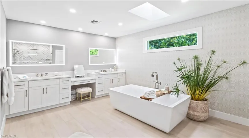 Full bath with wallpapered walls, vanity, a soaking tub, a skylight, and light wood-type flooring
