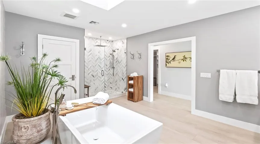 Bathroom with a stall shower, light wood-style flooring, a freestanding tub, recessed lighting, and a skylight
