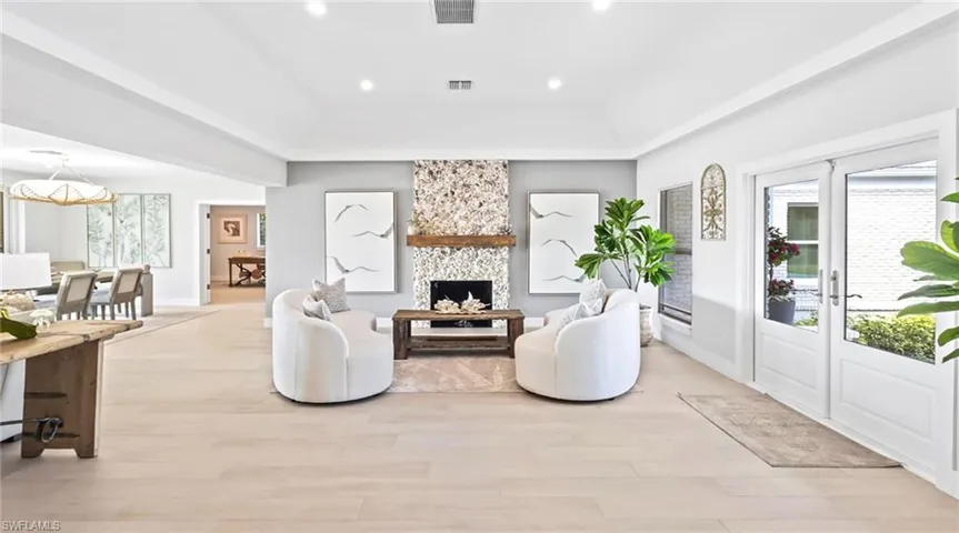 Living room with light wood-style floors, french doors, a large fireplace, a tray ceiling, and recessed lighting