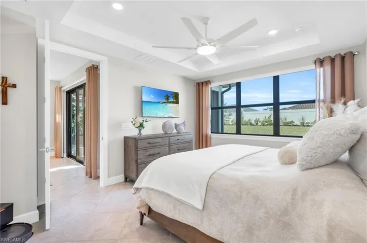 Bedroom with multiple windows, a tray ceiling, ceiling fan, and light tile patterned flooring