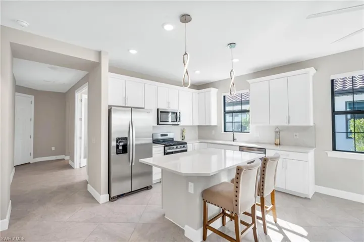 Kitchen featuring pendant lighting, white cabinetry, decorative backsplash, a center island, and stainless steel appliances