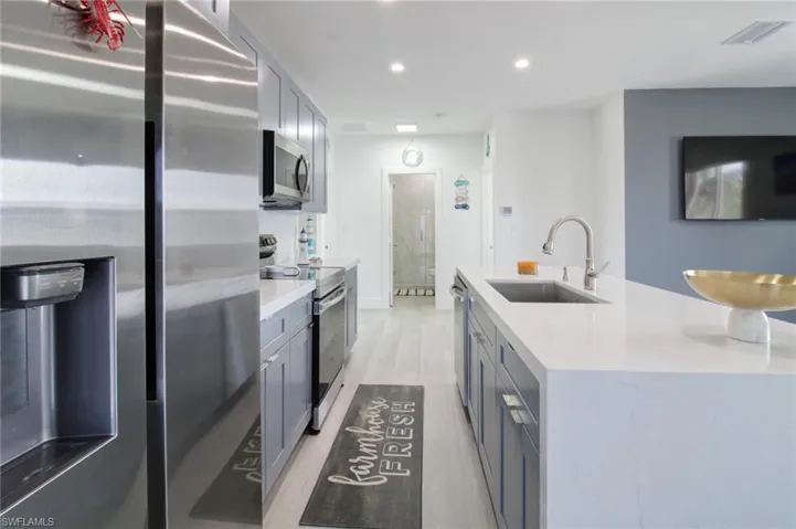 Kitchen featuring light hardwood / wood-style flooring, appliances with stainless steel finishes, a kitchen island with sink, gray cabinets, and sink