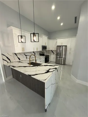 Kitchen with white cabinets, hanging light fixtures, stainless steel appliances, a peninsula, and light stone countertops