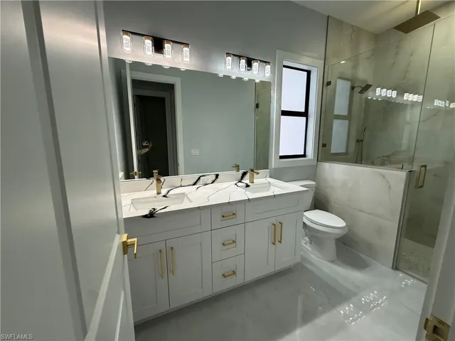 Bathroom with double vanity, a marble finish shower, and light marble finish floors