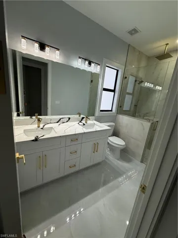 Bathroom with double vanity, a marble finish shower, and light marble finish floors