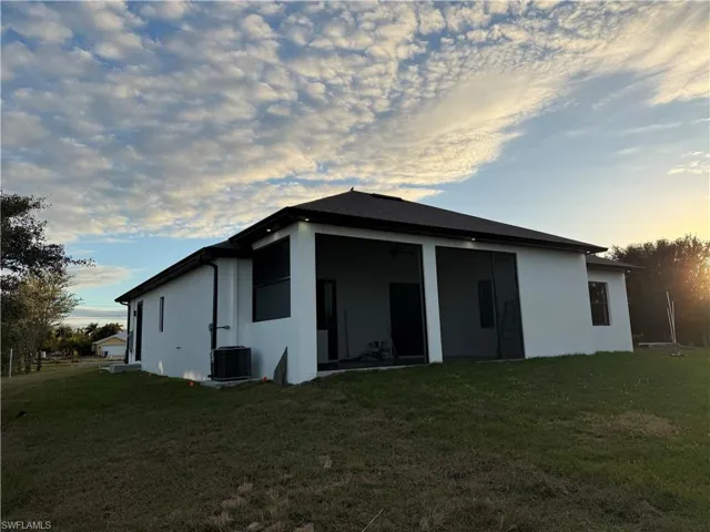 Back of house at dusk featuring stucco siding, a yard, and ceiling fan