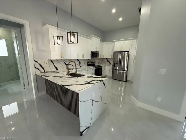 Kitchen with white cabinetry, decorative light fixtures, stainless steel appliances, light stone counters, and a peninsula