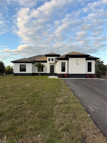 Prairie-style home featuring stucco siding, a front yard, and roof with shingles