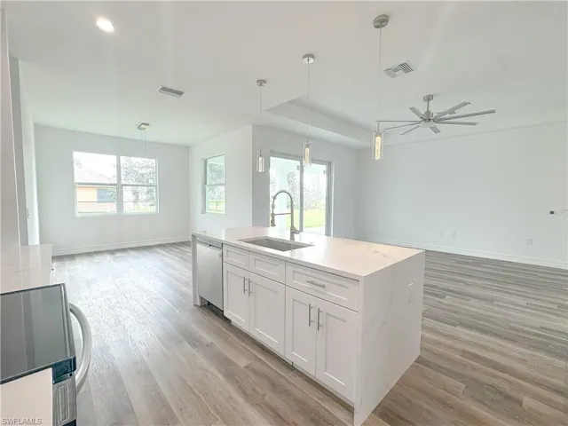 Kitchen featuring light stone countertops, sink, pendant lighting, white cabinets, and light hardwood / wood-style flooring