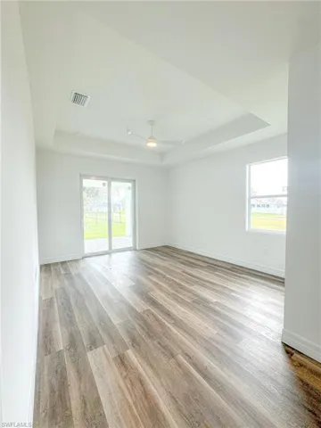 Master Bedroom unfurnished with access to outside,  featuring ceiling fan, a raised ceiling, light hardwood / wood-style flooring, and plenty of natural light