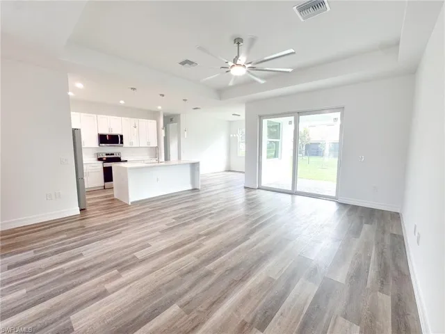 Unfurnished living room with sink, light hardwood / wood-style flooring, ceiling fan, and a raised ceiling