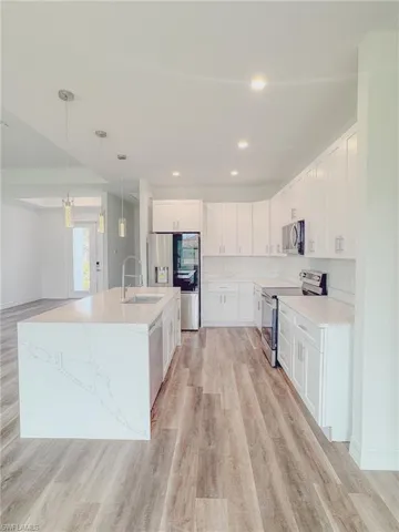 Kitchen with light hardwood / wood-style flooring, white cabinetry, stainless steel smart appliances, and pendant lighting