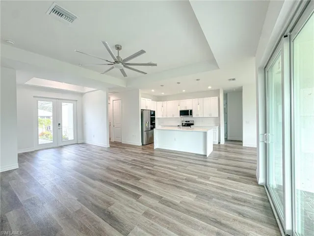Unfurnished living room featuring light hardwood / wood-style floors, Entry french door, Sliding door with lanai access, a tray ceiling, and ceiling fan