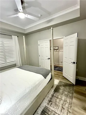 Bedroom featuring wood finished floors, a tray ceiling, ceiling fan, and crown molding