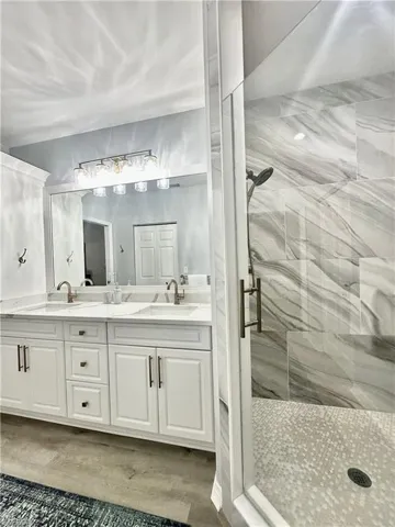 Full bathroom featuring a marble finish shower, double vanity, and light wood-style floors