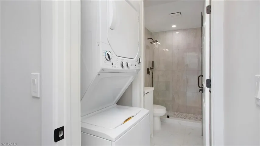 Bathroom with a shower stall, stacked washer and clothes dryer, light marble finish flooring, and recessed lighting