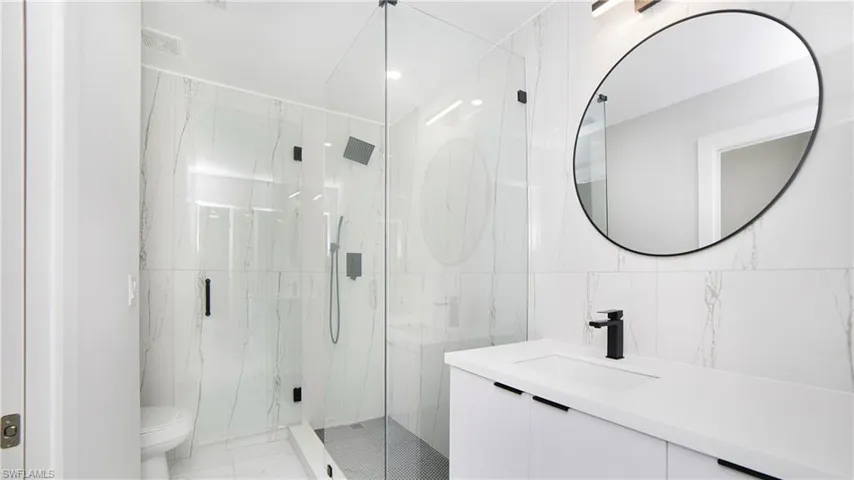 Full bathroom featuring tile walls, vanity, a marble finish shower, and light marble finish floors