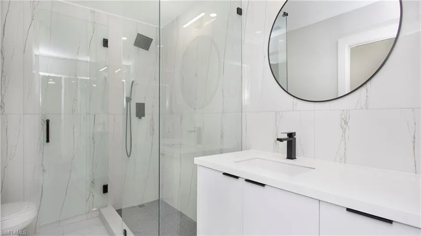 Full bath with tile walls, a marble finish shower, vanity, and light marble finish flooring