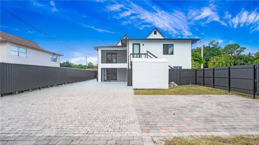 View of front of property with a balcony, stucco siding, a fenced backyard, and decorative driveway