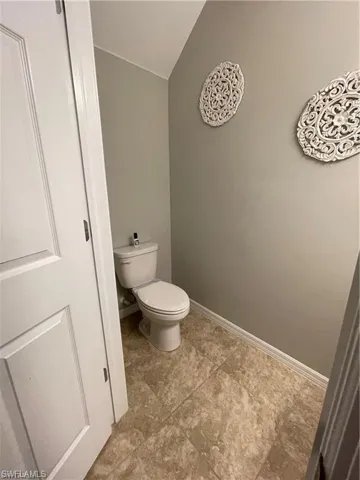 Bathroom with toilet, vaulted ceiling, and baseboards
