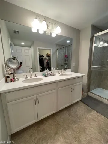 Bathroom featuring visible vents, a shower stall, double vanity, and a sink