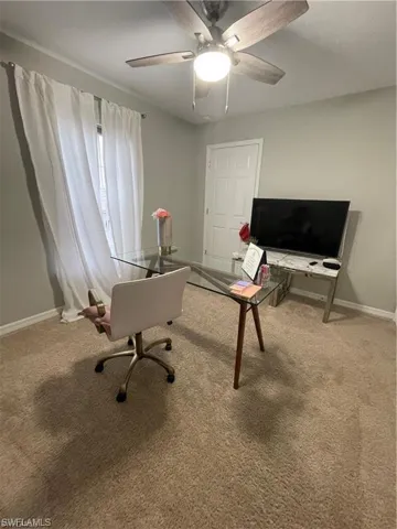 Carpeted home office featuring ceiling fan and baseboards