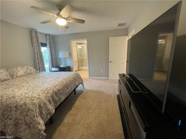 Bedroom with ensuite bath, light colored carpet, ceiling fan, baseboards, and visible vents