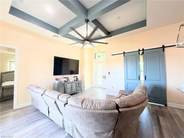 Living area featuring coffered ceiling, a barn door, beamed ceiling, a ceiling fan, and wood finished floors