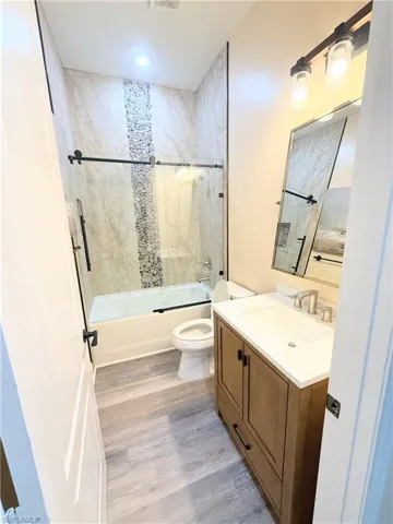 Bathroom featuring vanity, enclosed tub / shower combo, and light wood-style flooring