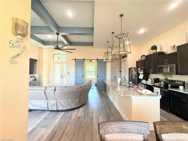 Kitchen featuring dark cabinets, open floor plan, stainless steel appliances, coffered ceiling, and decorative light fixtures
