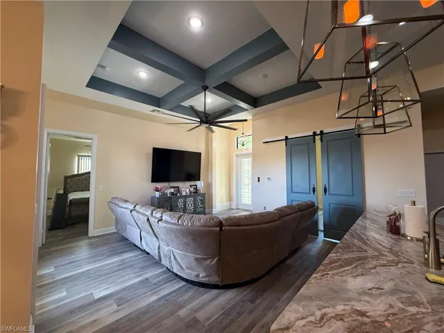 Living area featuring a barn door, coffered ceiling, ceiling fan, dark wood-type flooring, and beam ceiling