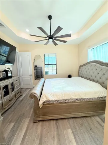 Bedroom with light wood-style flooring, ceiling fan, recessed lighting, and a tray ceiling